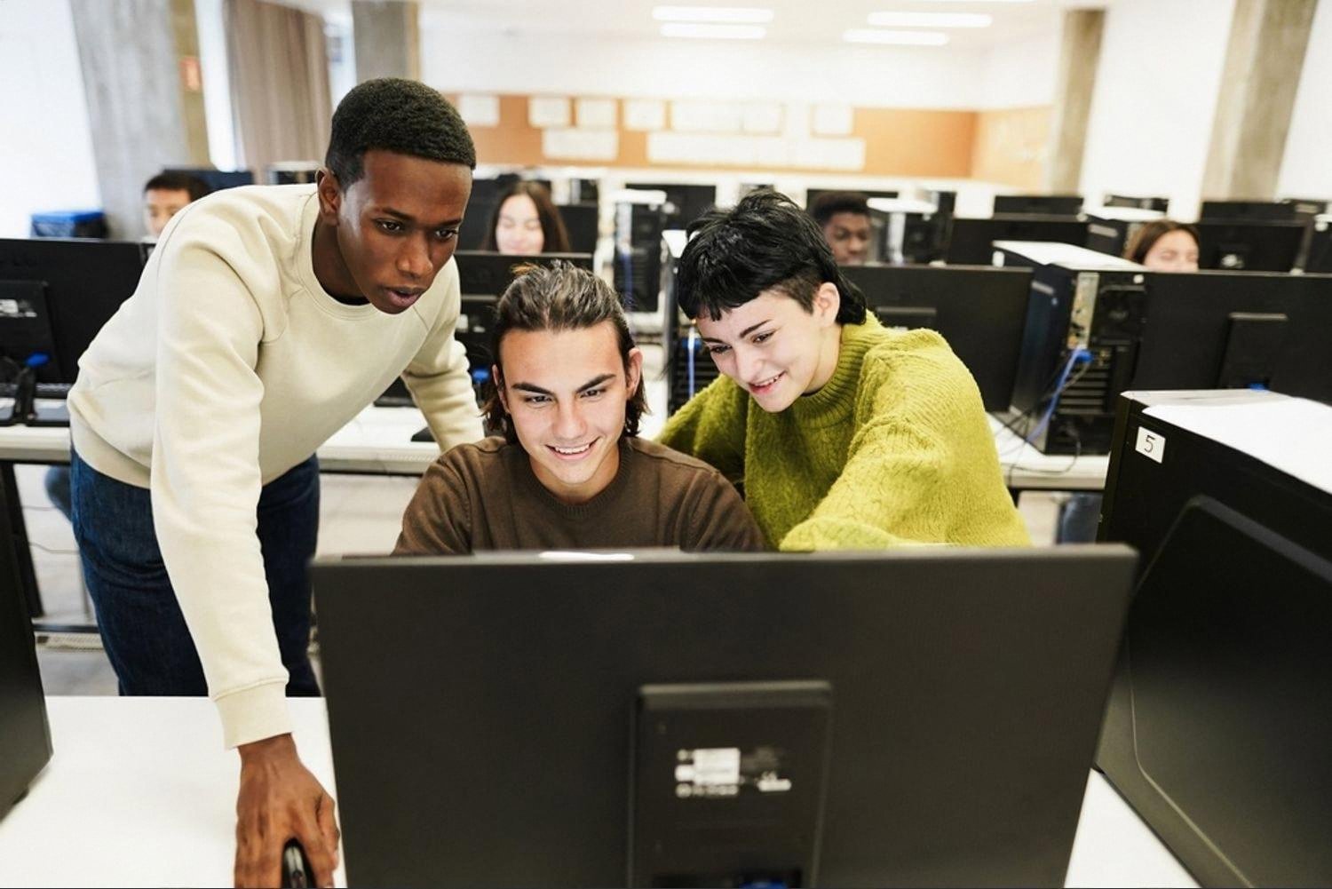 Three students working together at a desktop computer in a university AI lab